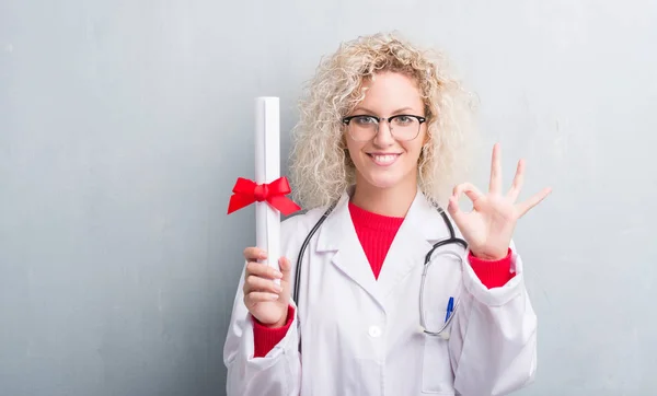 年轻的金发医生女人超过垃圾灰色墙持有学位做 标志与手指 优秀的标志 — 图库照片