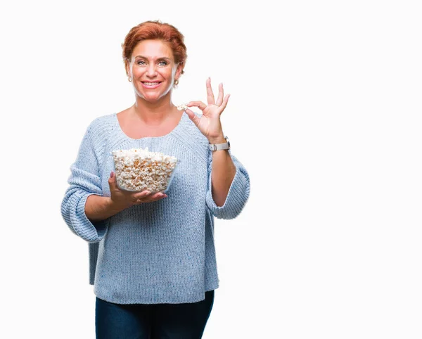 活跃的高级高加索红发妇女吃爆米花在孤立的背景与幸福的脸站着 面带微笑 自信的微笑显示牙齿 — 图库照片