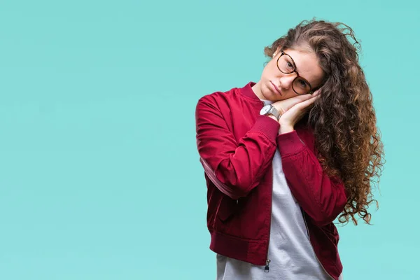 Beautiful brunette curly hair young girl wearing jacket and glasses over isolated background sleeping tired dreaming and posing with hands together while smiling with closed eyes.