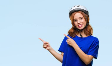 Gülümseyen ve iki elleri ve parmakları ile tarafına işaret kamera bakarak izole arka plan üzerinde bisikletçi kask giyen genç güzel kadın.