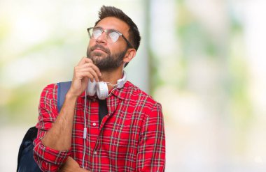 Üzerinde kulaklık ve sırt çantası giyiyor yetişkin İspanyol öğrenci adam arka plan çene düşünme hakkında soru, dalgın ifade üzerine el ile izole. Düşünceli yüzüyle gülümsüyor. Şüphe kavramı.