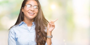 Kameraya bakarak yan el ve parmak ile işaret yüzünde kocaman bir gülümseme ile izole arka plan üzerinde gözlük takan genç güzel Arap kadın.