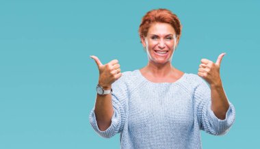 El ile pozitif jest yapıyor izole arka plan başarı işareti üzerinde kış kazak giyen Atrractive üst düzey beyaz Kızıl saçlı kadın başparmak gülümseyen ve mutlu. Neşeli bir ifadeyle, kazanan jest kameraya bakıyor.