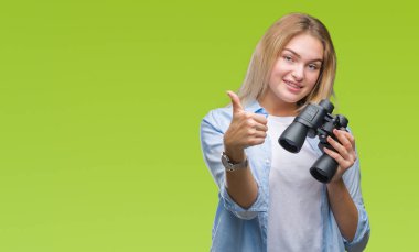 İzole arka plan üzerinde dürbün ok işareti, başparmak ile parmak, mükemmel işareti yapıyor kocaman bir gülümseme ile mutlu tutan genç beyaz kadın