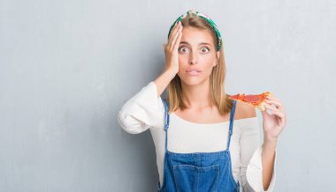 Güzel genç kadın baş, el ile vurguladı pepperoni pizza dilimi yemek grunge gri duvar yüzünden şok utanç ve sürpriz suratla, öfkeli ve sinirli. Korku ve hata için üzgün.