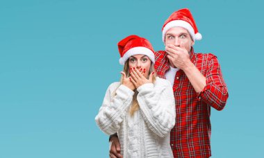Genç çift aşık izole arka plan ağız hata için elleriyle kapsayan şok üzerinde Noel şapka giyiyor. Gizli kavramı.