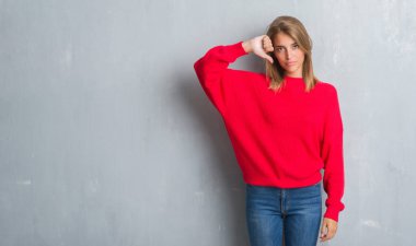 Grunge gri üzerinde duran güzel genç kadın duvar giyen kış kazak kızgın yüzü, eksi işareti aşağı antipati başparmak ile gösterilen, ret kavramı ile