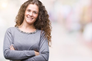 Güzel esmer kıvırcık saçlı Genç kız kameraya bakarak çapraz silah ile gülümseyen izole arka plan mutlu yüz üzerinden bir kazak giyiyor. Olumlu bir kişi.