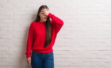 Mahcup ifadeyle parmaklarımın arasından seyir üzerinde tuğla duvar yüz ve gözler el ile kapsayan şok bakmak Genç Çinli kadın.