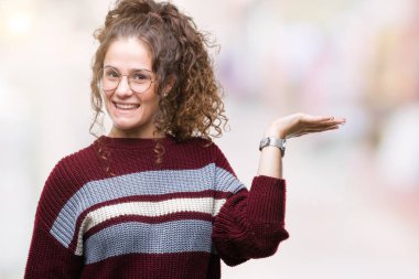 Güzel esmer kıvırcık saçlı Genç kız neşeli sunulması ve kameraya bakarak avucunun ile işaret gülümseyen izole arka plan üzerinde gözlük.