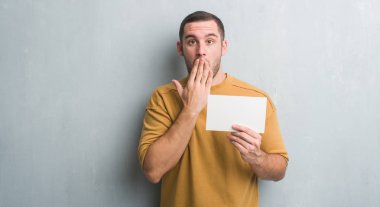 Hata, korku, sessizlik içinde gizli kavramı korkmuş ifade için utanç ile boş kartı kapak ağız eliyle tutarak gri grunge duvarın üzerinden beyaz delikanlı şok