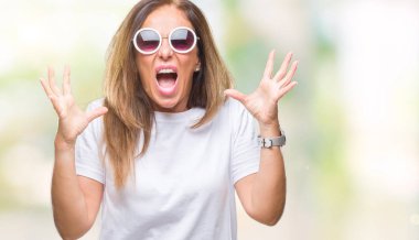 Orta yaş İspanyol kadın üzerinde moda güneş gözlüğü takıyor arka plan deli izole ve deli bağırarak ve agresif ifade ve silah kaldırdı bağırıyor. Hayal kırıklığı kavramı.