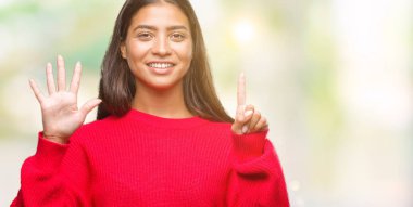 Genç güzel Arap kadın giyiyor kış kazak gösterilen ve parmakları ile işaret izole arka plan üzerinde kendinden emin ve mutlu gülümseyerek süre 6 numara.