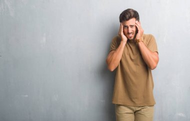 Yakışıklı genç adam baş baş ağrısı için el ile gri grunge duvarın üzerinden çünkü stres. Migren muzdarip.