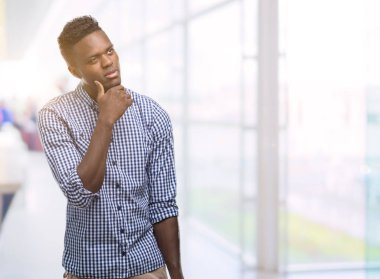 Çene düşünme hakkında soru, dalgın ifade üzerine el ile mavi gömlek giymiş genç Afro-Amerikan adam. Düşünceli yüzüyle gülümsüyor. Şüphe kavramı.