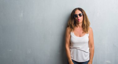 Orta yaş İspanyol kadın balık yapma güneş gözlüğü takıyor gri duvarın üzerinden yüz dudaklı, çılgın ve komik bir jest. Komik ifade.