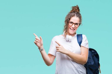 Gülümseyen ve iki elleri ve parmakları ile tarafına işaret kamera bakarak izole arka plan üzerinde sırt çantası ve kulaklıklar giyen genç esmer öğrenci kız.