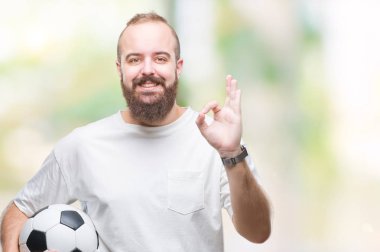 Parmak, mükemmel sembolü ile ok işareti yapıyor izole arka plan üzerinde futbol futbol topu tutan genç beyaz hipster adam