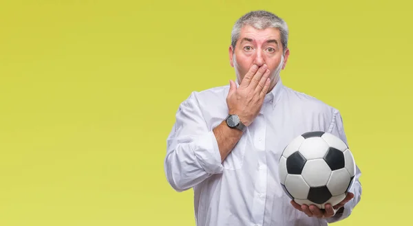 Handsome senior man holding soccer football ball over isolated background cover mouth with hand shocked with shame for mistake, expression of fear, scared in silence, secret concept