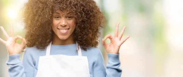 African american shop owner woman wearing an apron doing ok sign gesture with both hands expressing meditation and relaxation
