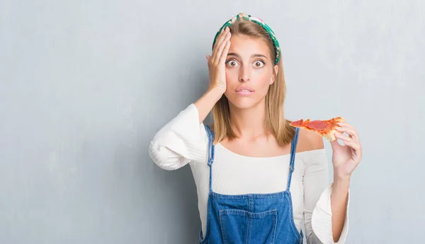 頭の上の手を強調したペパロニのピザのスライスを食べるグランジ灰色の壁に美しい若い女性が恥と驚きの顔でショックを怒っているとイライラします 恐怖と動揺の間違い — ストック写真