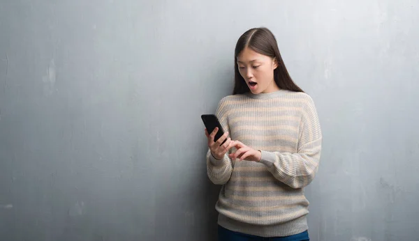灰色墙上的中国年轻女子看着智能手机吓坏了惊讶的脸 害怕和兴奋的表情恐惧表达 — 图库照片