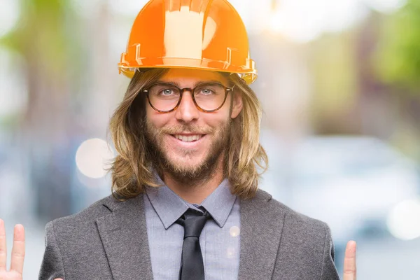 年轻英俊的建筑设计男子长头发戴安全头盔在孤立的背景显示和指向六的手指 而微笑着自信和快乐 — 图库照片