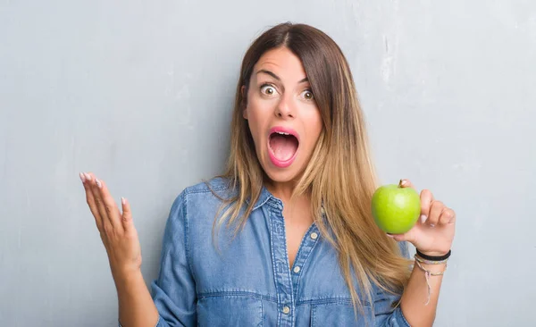 灰色のグランジの若い成人女性壁食べて笑顔で叫び 手を上げた勝利を祝ってみずみずしいグリーンアップル非常に幸せと興奮 受賞式 — ストック写真