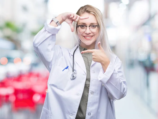 Young blonde doctor woman over isolated background smiling making frame with hands and fingers with happy face. Creativity and photography concept.