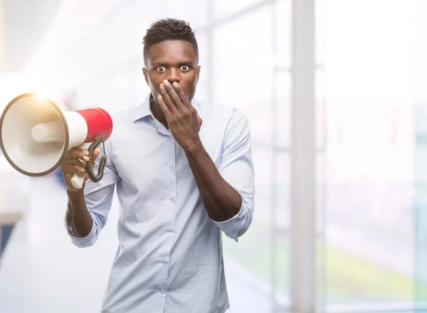 Young african american man holding megaphone cover mouth with hand shocked with shame for mistake, expression of fear, scared in silence, secret concept