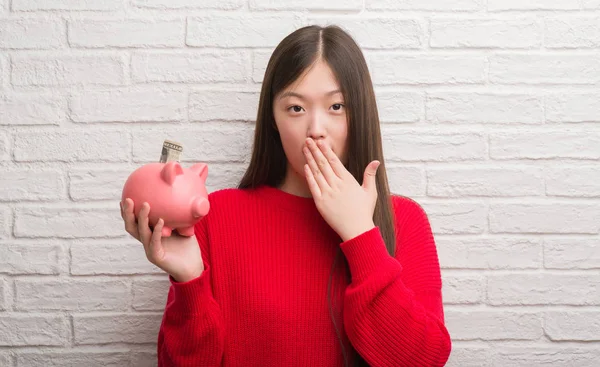 Joven Mujer China Sobre Pared Ladrillo Sosteniendo Boca Cubierta Alcancía — Foto de Stock