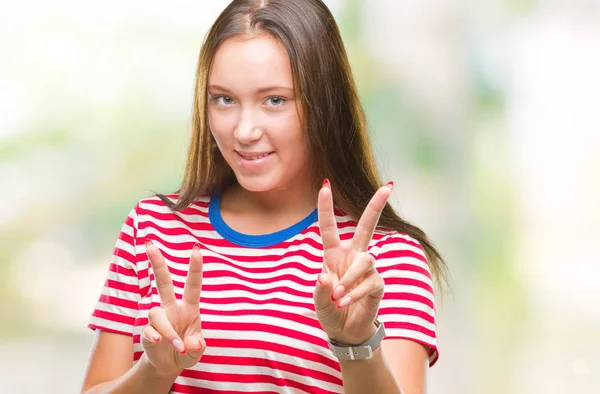 勝利のサインをやって指を表示するカメラを笑みを浮かべて孤立の背景の上の若い白人の美しい女性 — ストック写真