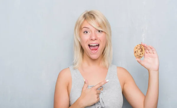 非常に幸せな手と指で指しているチョコレート クッキーを食べて灰色グランジ壁を越えて白人の大人の女 — ストック写真