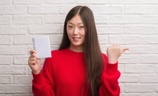 Joven Mujer China Sobre Pared Ladrillo Mostrando Cuaderno Blanco Señalando —  Fotos de Stock