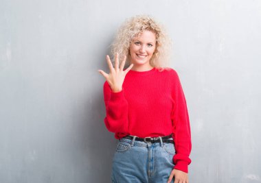 Gösterilen ve parmakları ile işaret grunge gri arka plan üzerinde Kıvırcık saçlı sarışın genç kadın kendinden emin ve mutlu gülümseyerek süre beş numara.