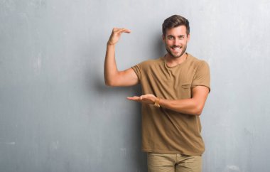 Yakışıklı genç adam gri grunge duvar eller eller büyük gösterilen ve büyük boy işareti, ölçü birimi sembolü ile üzerinden. Kameraya bakarak gülümsüyordu. Ölçüm kavramı.
