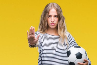 Açık eliyle dur işareti ile ciddi ve kendine güvenen ifade, savunma jest yapıyor izole arka plan üzerinde futbol futbol topu tutan güzel genç sarışın kadın