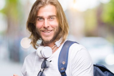 Genç yakışıklı turist adam uzun saçlı giyen ile sırt çantası gülümseyen ve iki elleri ve parmakları ile tarafına işaret kamera bakarak izole arka plan üzerinde.