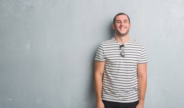 Beyaz delikanlı gri grunge duvarın yüzünde mutlu ve güzel bir gülümseme ile üzerinden. Şanslı kişi.