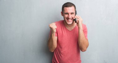 Duygu tezahürat Genç beyaz adam gurur çığlık ve zafer ve başarı çok heyecanlı, kutluyor telefonda konuşurken gri grunge duvarın üzerinden