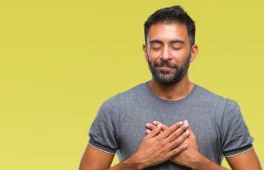 Göğüs kapalı gözler ve yüzünde minnettar jest ile yetişkin İspanyol adam ile gülümseyen izole arka plan üzerinde eller. Sağlık kavramı.