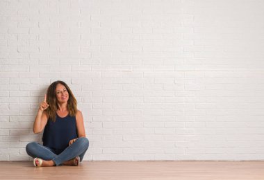 Orta yaş İspanyol kadın yerdeki beyaz tuğla duvar işaret parmağı üzerinde başarılı fikirle oturuyor. Çıktıktan ve mutlu. Bir numara.