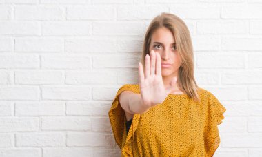 Güzel genç kadın ile beyaz tuğla duvarın üzerinden açık el dur işareti ile ciddi ve kendine güvenen ifade, savunma hareketi yapıyor