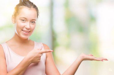 Hayret ve el ile sunulması ve parmak ile işaret ederken kameraya gülümseyen izole arka plan üzerinde beyaz genç güzel kadın.