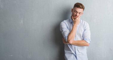 Yorgun ve bıkkın ile depresyon sorun Çapraz kollar ile duvar gri grunge düşünme seyir üzerinde genç redhead iş adamı.