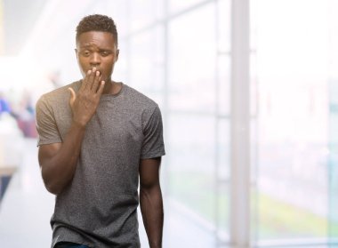 Gri t-shirt giyen genç Afro-Amerikan adam el ağzıyla kapsayan yorgun esneme sıkılmış. Restless ve uyku hali.