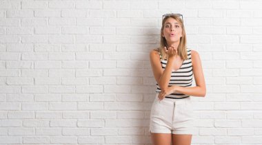Bir öpücük el ile güzel ve seksi olmak hava üfleme kamera bakıyor beyaz tuğla duvarın üzerinden genç güzel sarışın kadın. Aşk ifade.