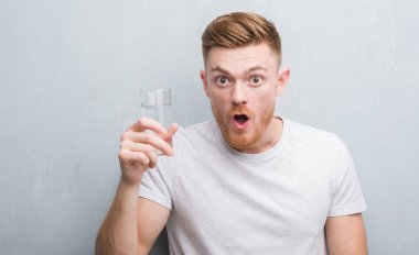 Gri grunge duvar içme suyu bir sürpriz yüz, korkuyor ve heyecanlı korku ifadesi ile şok korkmuş genç Kızıl saçlı adam