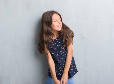 Genç İspanyol çocuk grunge gri duvar uzak tarafına yüzünde, doğal ifade gülümseme ile seyir için. Kendine güvenen gülüyor.