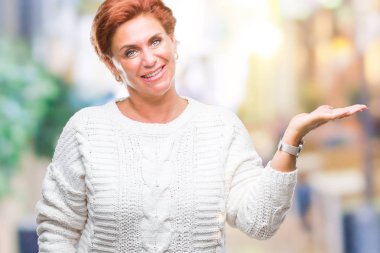 Neşeli sunulması ve kameraya bakarak avucunun ile işaret gülümseyen izole arka plan üzerinde kış kazak giyen Atrractive üst düzey beyaz Kızıl saçlı kadın.